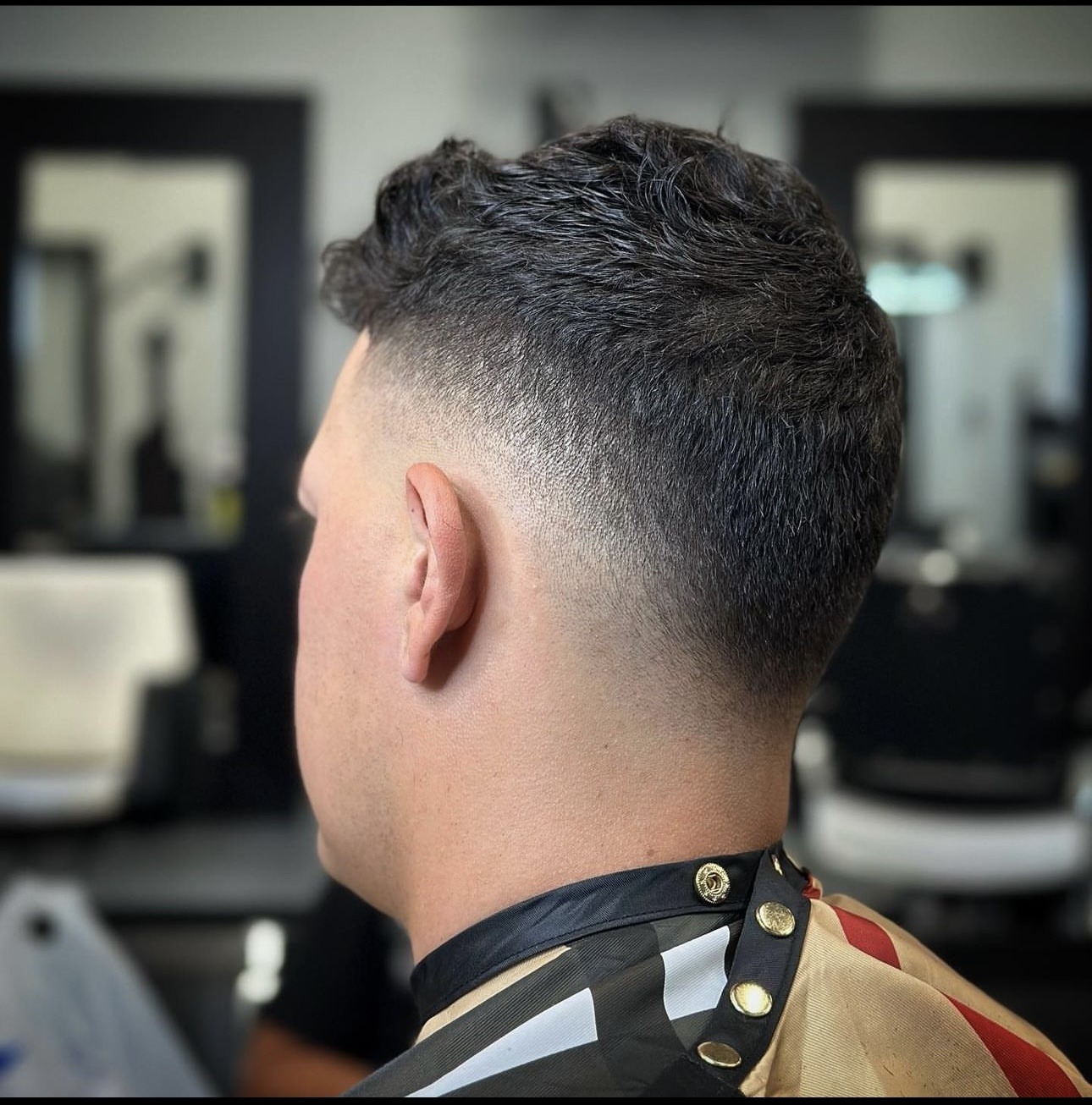 A man with a fade haircut sits in a barber shop, surrounded by tools and mirrors.