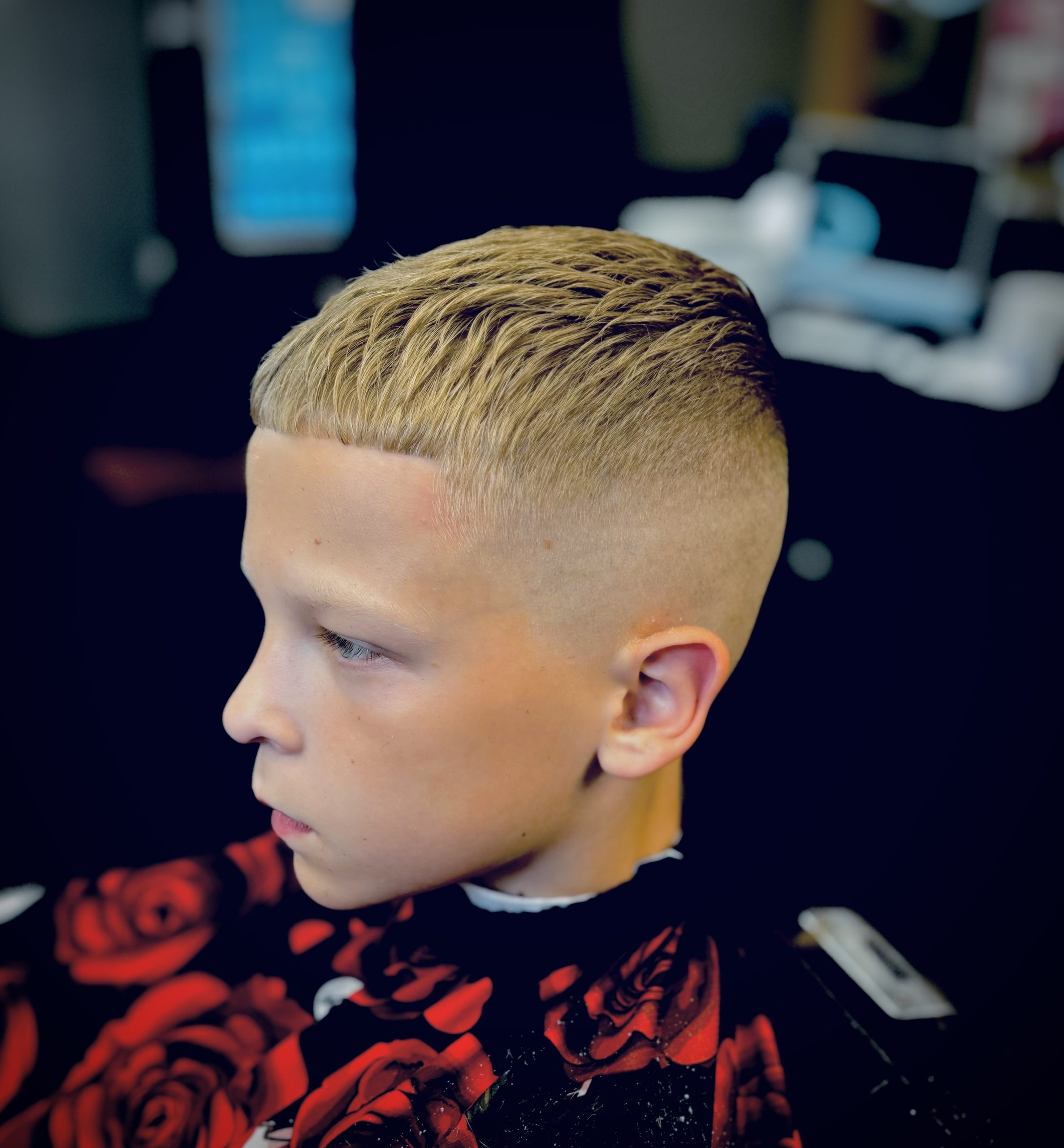 A young boy with a neat short haircut is seated in a barber chair.
