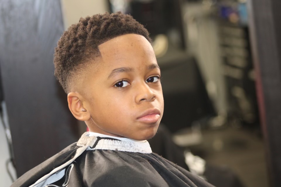 A young boy sits in a barber’s chair, smiling as his hair was cut by a professional barber.